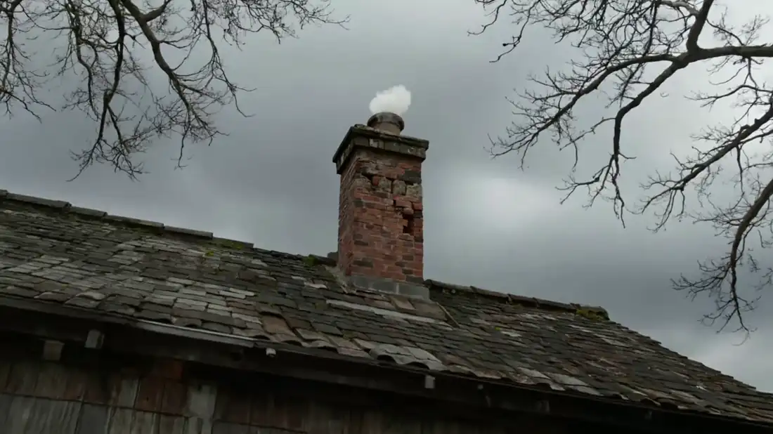 A brick chimney with smoke rising, on a slate roof under an overcast Ohio sky